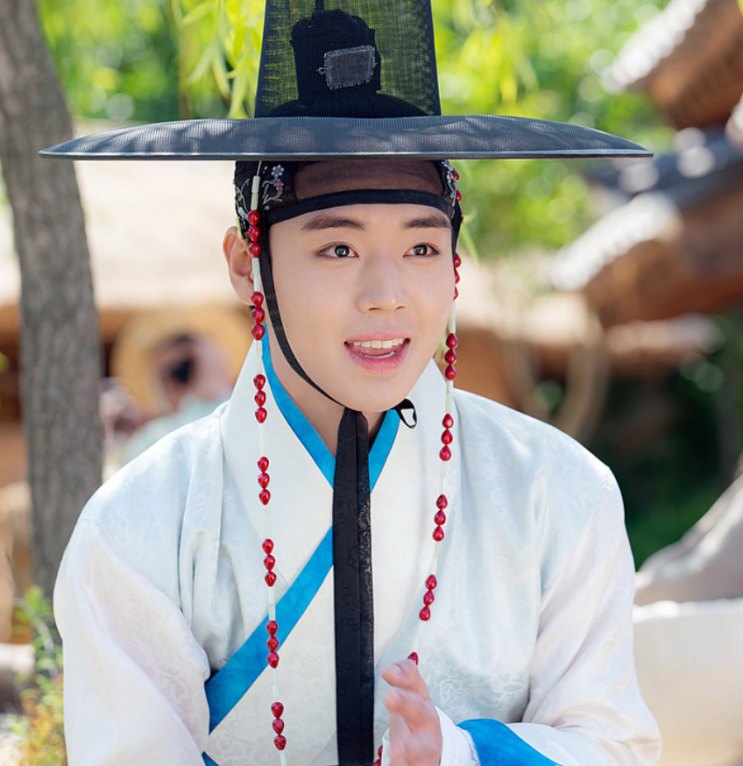 Park Ji-hoon de hanbok claro e chapéu tradicional, sorrindo em cena da série