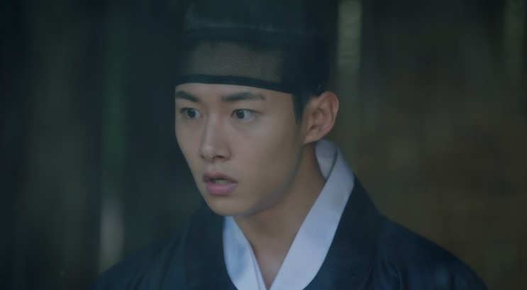 Seo Ji-hoon de hanbok escuro, com expressão surpresa