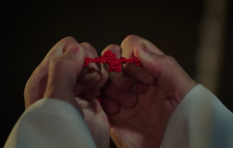 Duas mãos segurando um nó de cordão vermelho entre os dedos