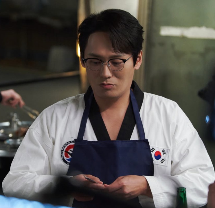 Choi Dae-hoon de uniforme de taekwondo (dobok) e avental, como Seong Han-su