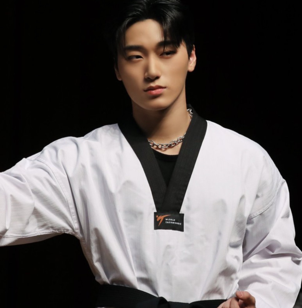 Choi San de dobok branco de taekwondo com faixa preta, em pose de golpe