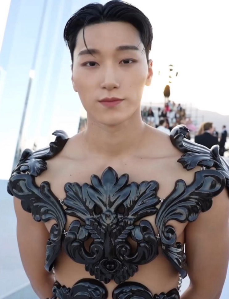 Choi San de cabelo penteado para trás, usando um peitoral preto com desenhos em relevo