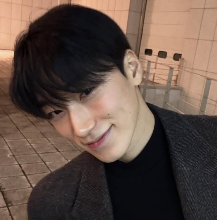 Selfie de Choi San sorrindo à noite, de casaco cinza sobre gola alta preta