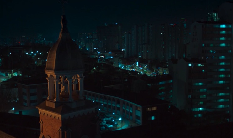 Vista do alto da torre da igreja, com a cidade iluminada ao fundo, em Dark Nuns