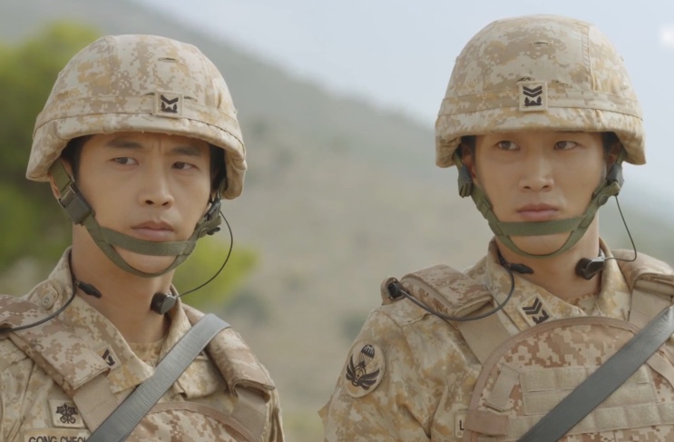 Dois soldados da equipe Alfa lado a lado, de capacete, num morro