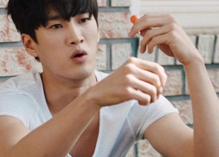 Ahn Bo-hyun de camiseta branca, agachado ao lado de um muro de tijolos