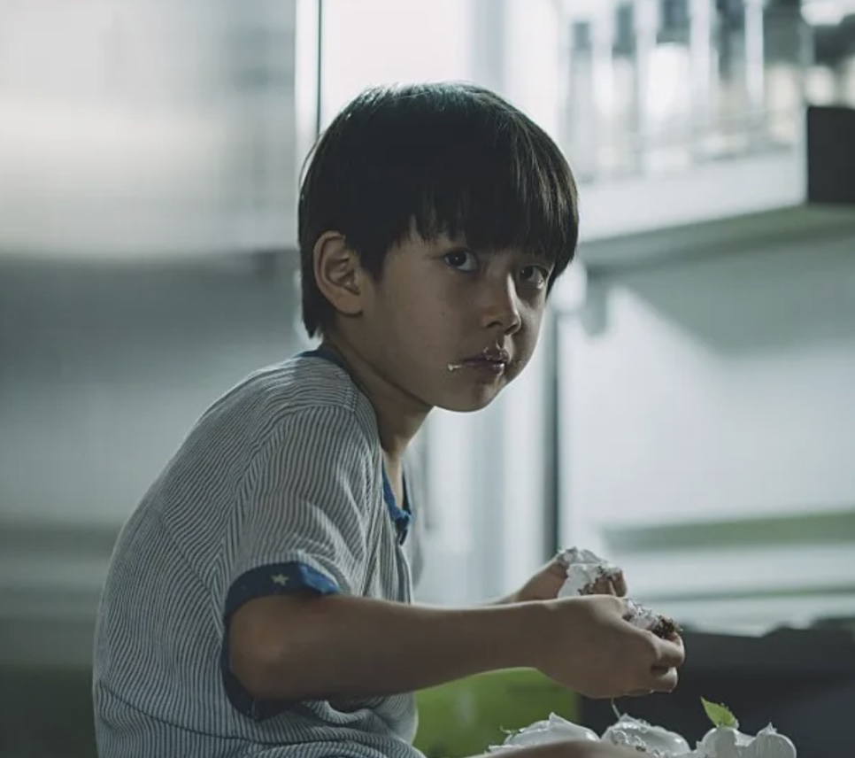 Jung Hyeon-jun criança, no papel do Da-song em Parasita, comendo um doce, com creme no canto da boca