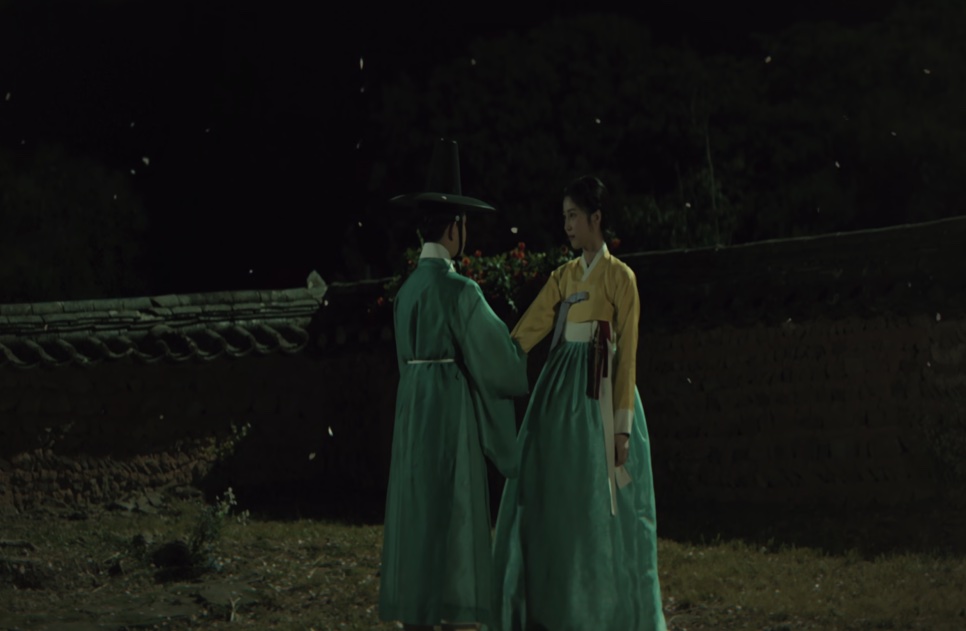 O jovem Cho Won e a jovem Cho Yun, de hanbok amarelo, frente a frente num jardim à noite, em Escândalo e Intriga