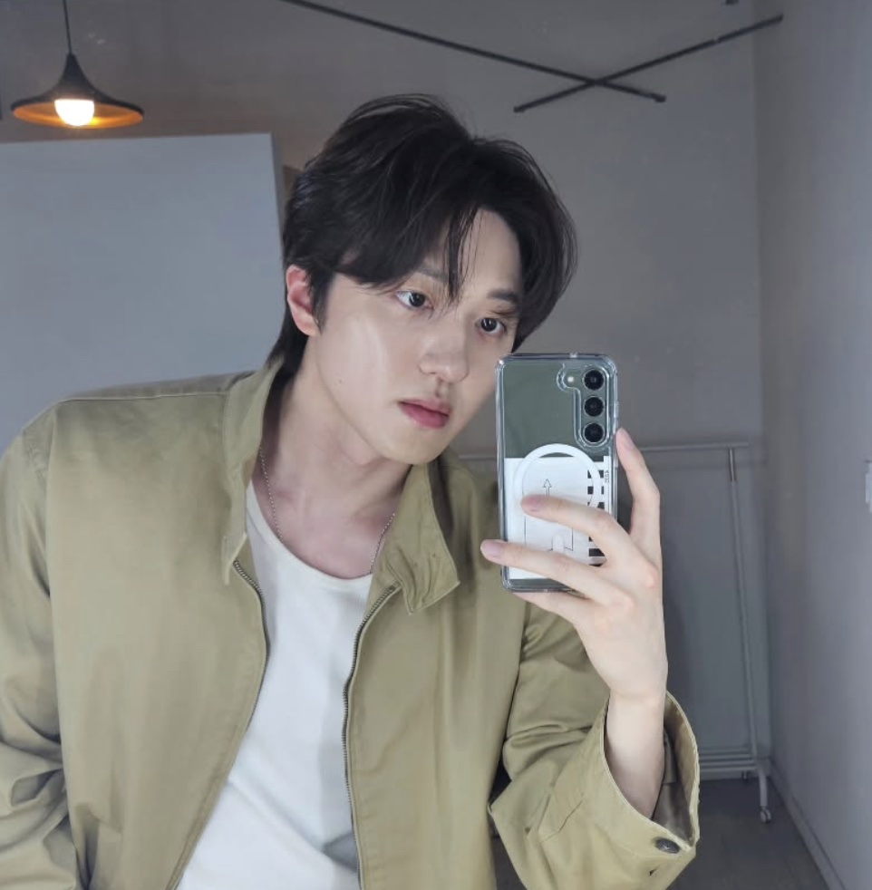 Chani, do grupo de K-pop SF9, tirando uma selfie no espelho, de jaqueta cáqui