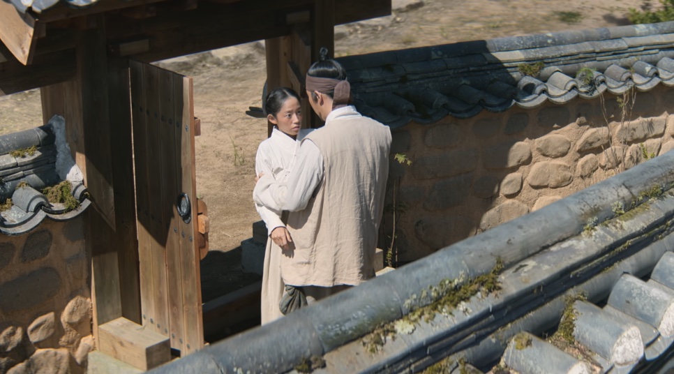 Eun-sil conversando com um homem junto ao portão de um pátio com muro de pedra, em Escândalo e Intriga