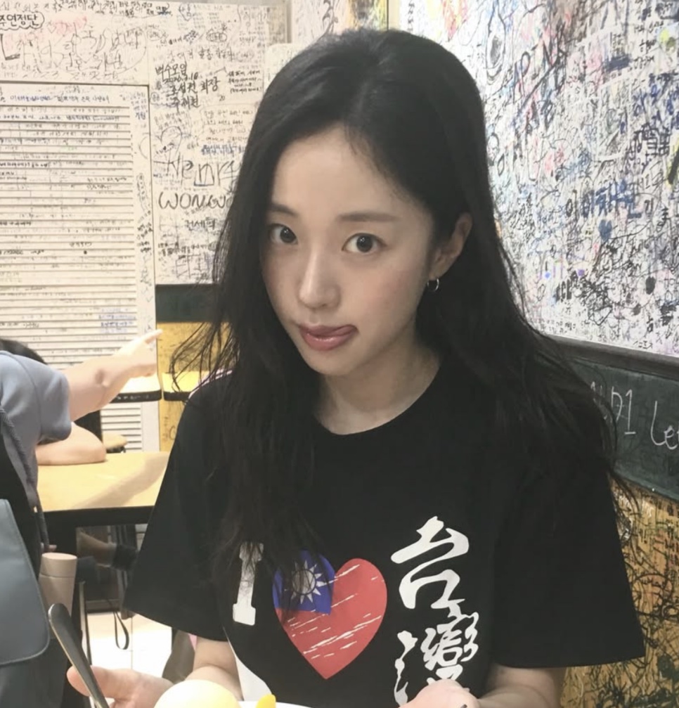 Kim Ji-an de camiseta preta, sentada num restaurante com as paredes cobertas de recados escritos à mão