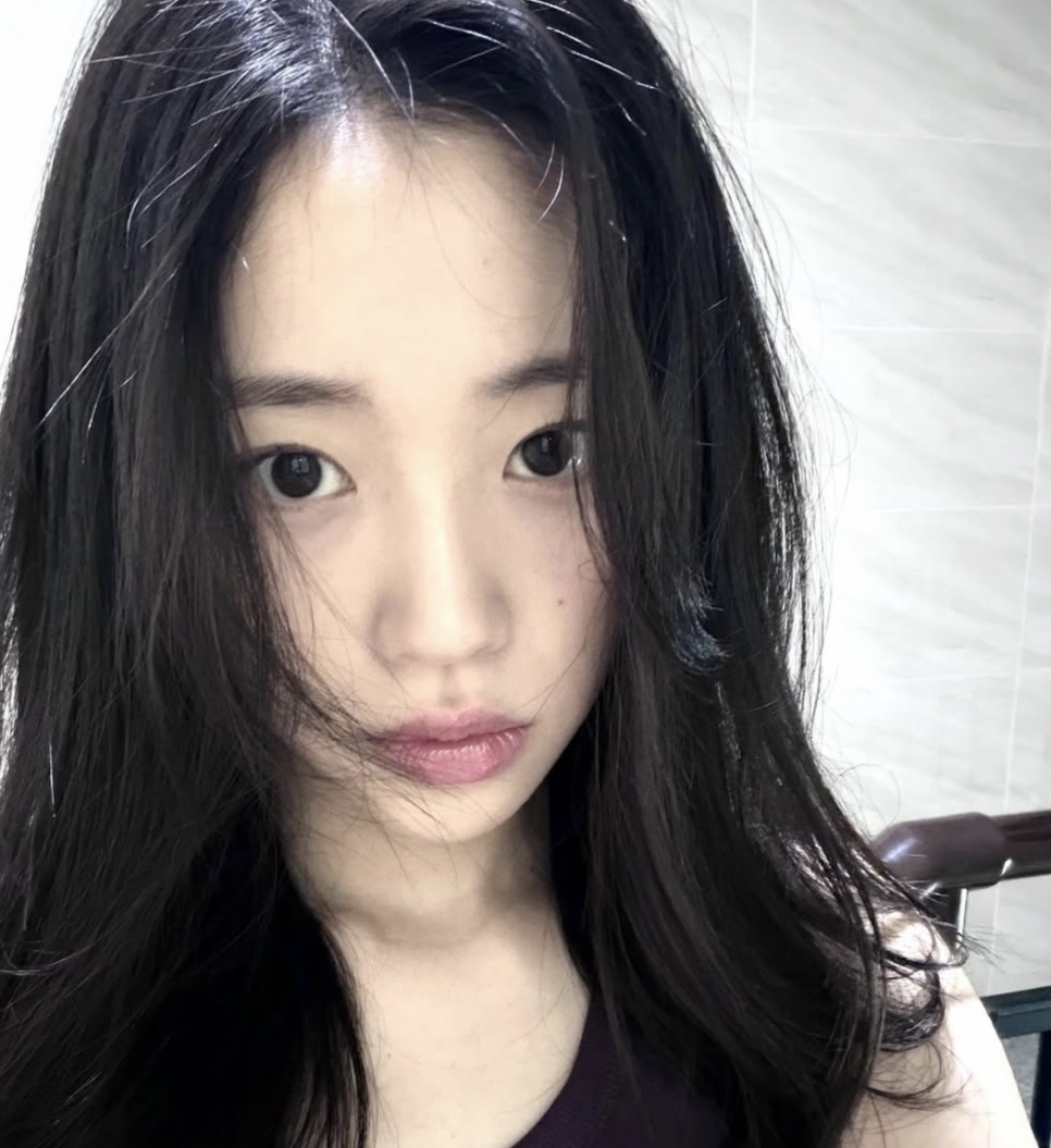 Selfie da Kim Ji-an com o cabelo solto, sem maquiagem, em frente a uma parede clara