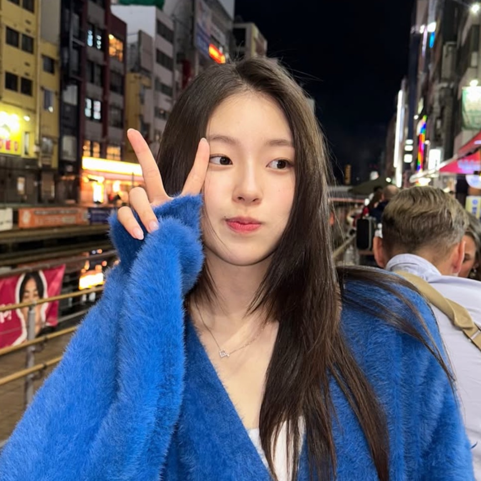 Shin Youn-ha, a atriz que faz a So-ok em Escândalo e Intriga, de casaco azul peludo, fazendo sinal de V ao lado do rosto numa rua à noite