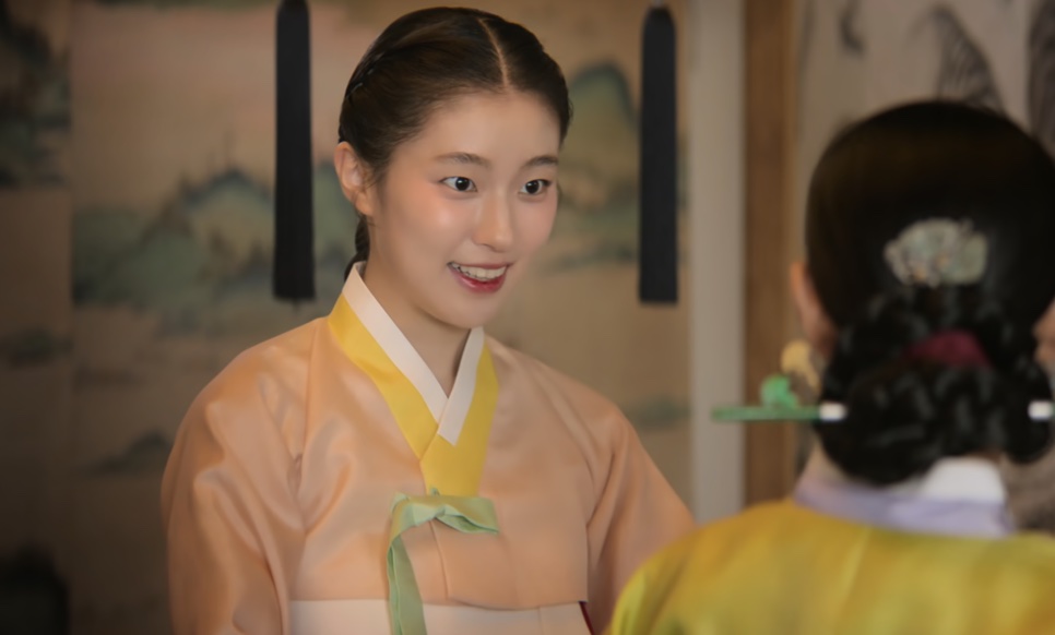 So-ok, de hanbok cor de pêssego com laço verde, sorrindo para uma mulher de costas, em Escândalo e Intriga
