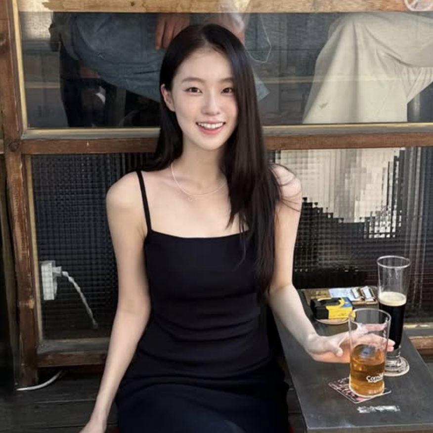 Shin Youn-ha de vestido preto de alcinha, sorrindo sentada numa mesa de bar