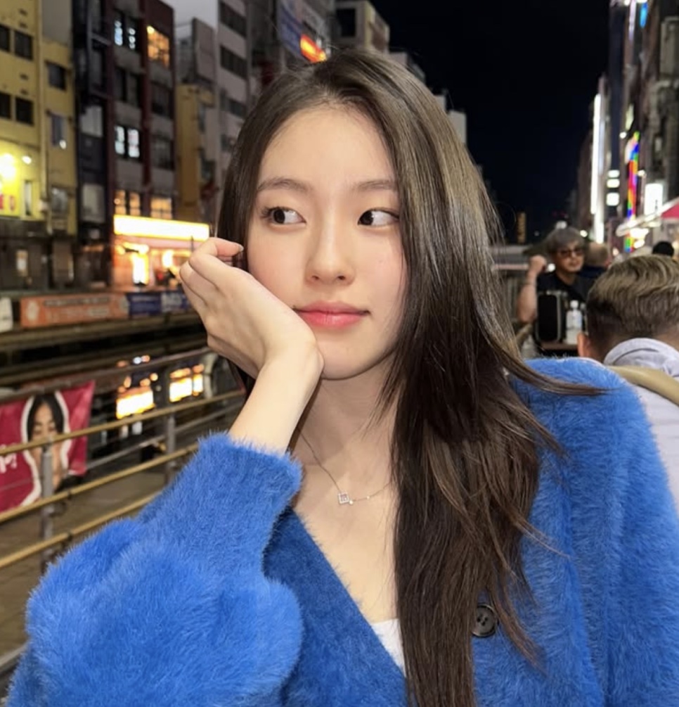 Shin Youn-ha de casaco azul, com a mão no rosto, olhando para o lado numa rua à noite