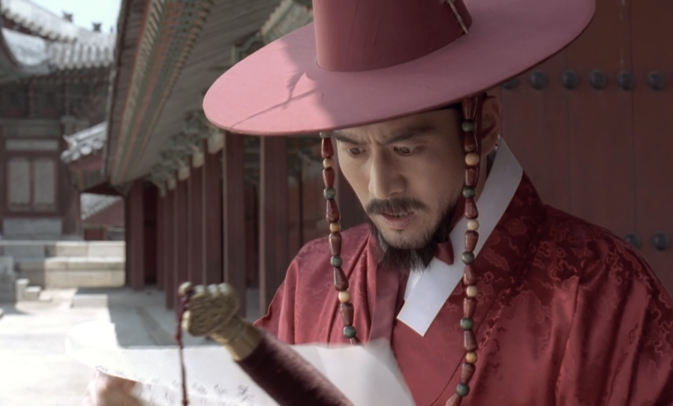 Um homem de roupa vermelha e chapéu vermelho de abas largas lendo um papel no pátio de um palácio, em Untold Scandal