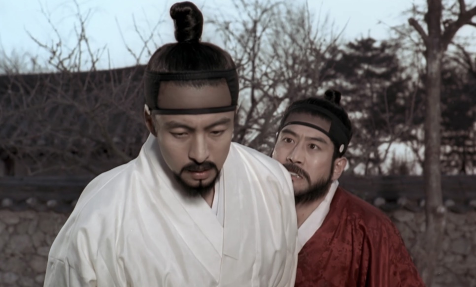 O Jo-won, de cabelo preso em coque e roupa branca, com um homem de vermelho logo atrás dele, em Untold Scandal