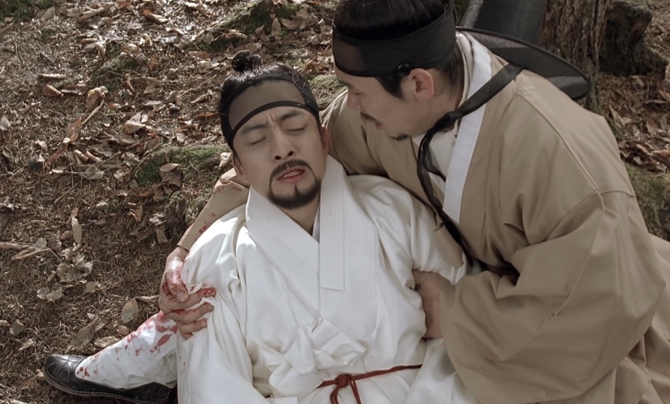 O Jo-won ferido e sangrando, caído no chão e amparado por um homem de chapéu preto, em Untold Scandal