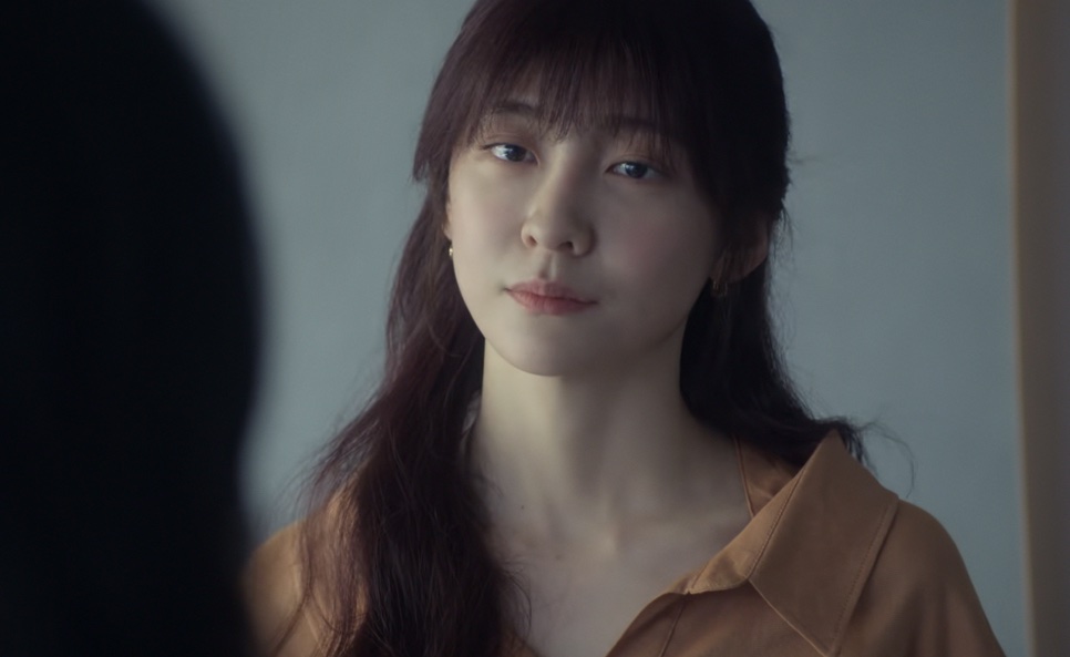 Cheon Sang-yeon (Park Ji-hyun) de camisa laranja, com o olhar sério, diante de alguém