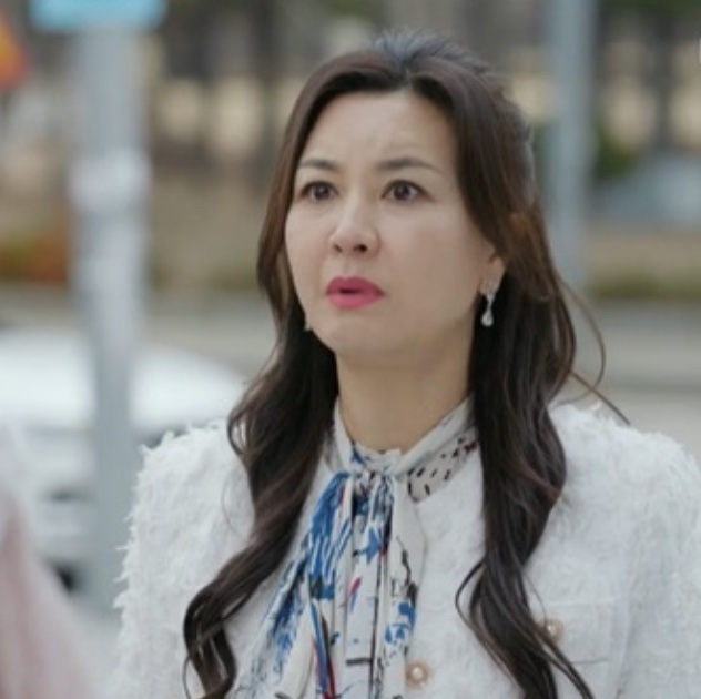Kim Hye-sun de casaco branco e lenço estampado na rua, em A Bela e o Sr. Romântico