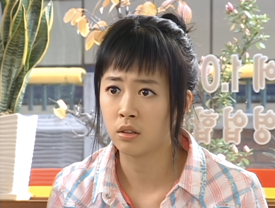 Shin Ji-soo de franja e camisa xadrez com cara de espanto, no papel de Na Jong-chil