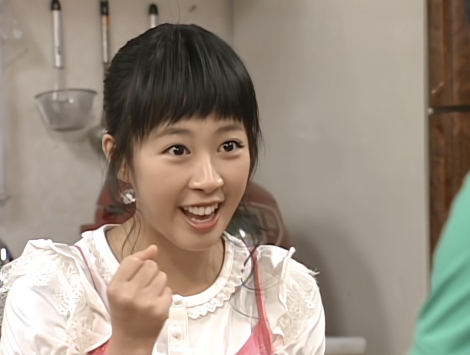 Shin Ji-soo sorrindo animada numa cozinha, no papel de Na Jong-chil