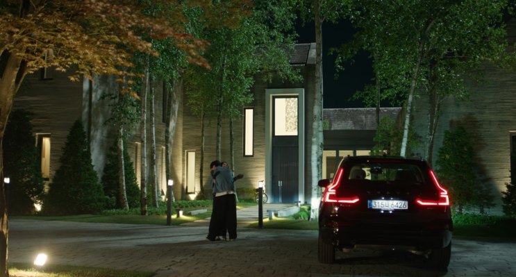 Cena noturna: uma pessoa parada ao lado de um carro na entrada iluminada da casa
