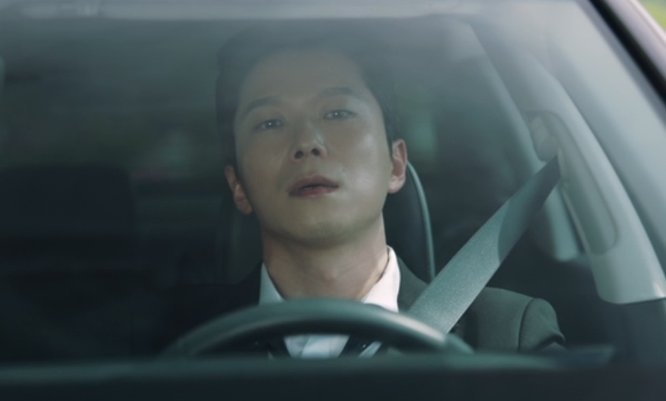 Close do Han Jong-hyun dirigindo, de cinto de segurança e gravata, em Flex X Cop 2