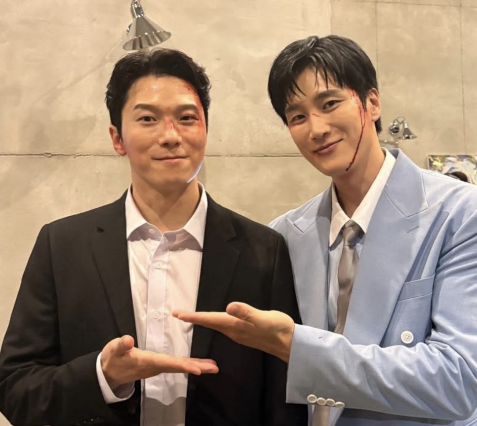 Moon Jin-seung com sangue cenográfico no rosto, posando ao lado de um colega de elenco nos bastidores