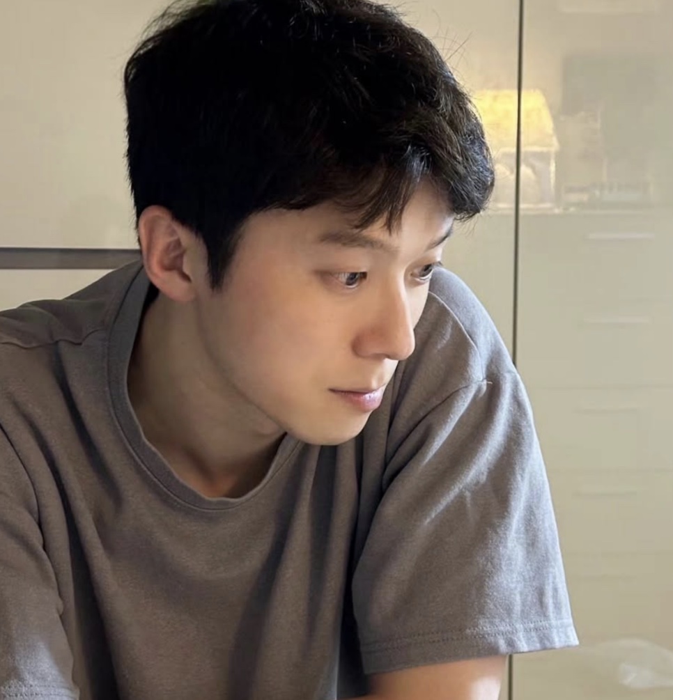 Moon Jin-seung de camiseta cinza, de perfil, olhando para baixo