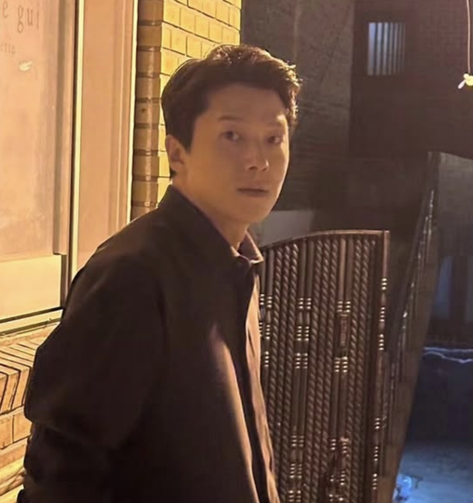Moon Jin-seung de jaqueta escura, olhando para a câmera numa rua à noite