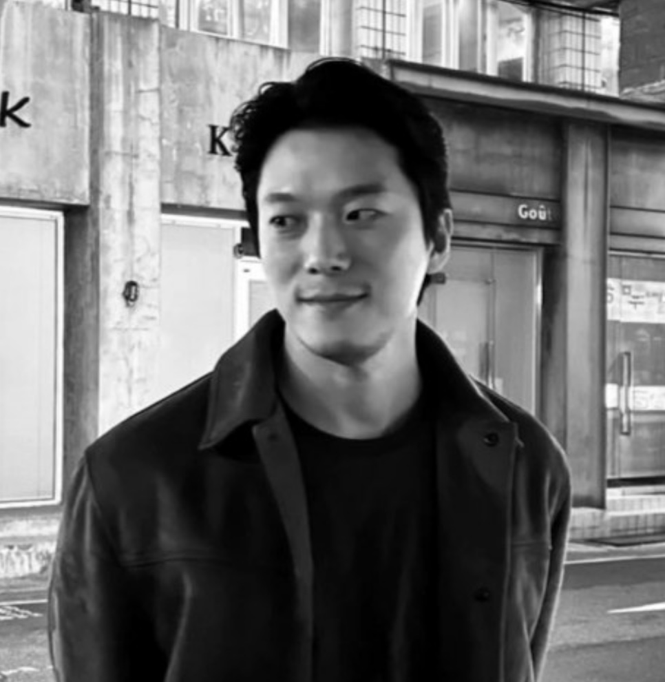 Foto em preto e branco do Moon Jin-seung de jaqueta de couro, parado numa calçada