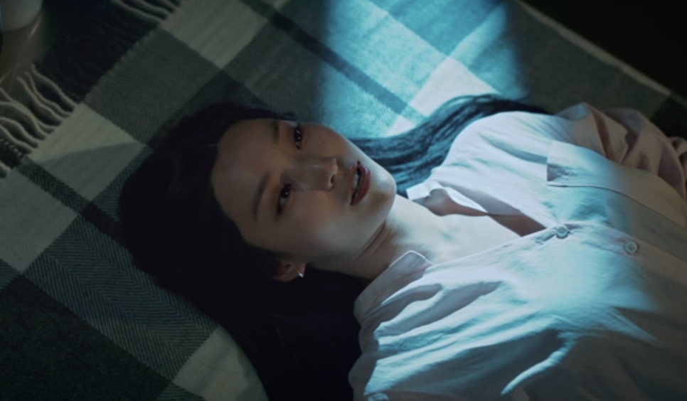 Song A-reum de camisa branca, deitada sobre uma manta xadrez, sob uma luz azulada