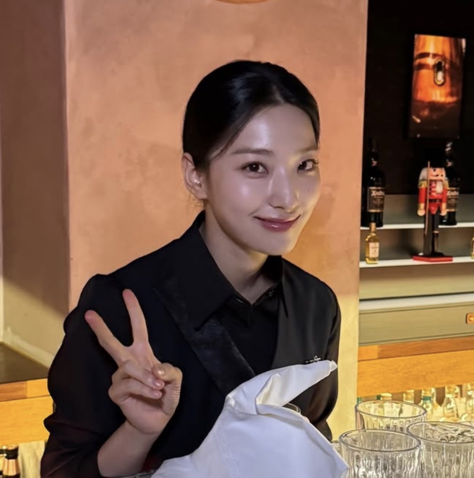 Lee Sae-rom com o uniforme de bartender da Song A-reum, fazendo sinal de paz nos bastidores de Flex X Cop