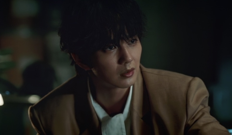 Yoo Seung-ho de blazer marrom, no papel do escultor Yoo Seong-won, numa cena escura