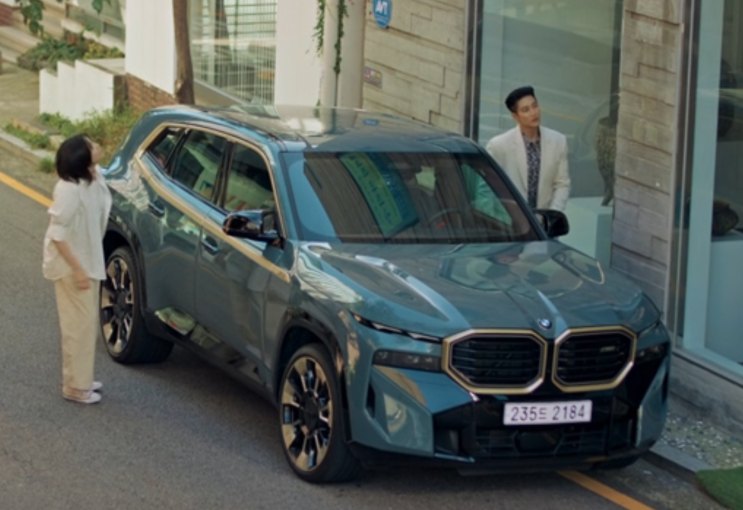 BMW XM azul-clara estacionada em frente a um prédio, com duas pessoas ao lado