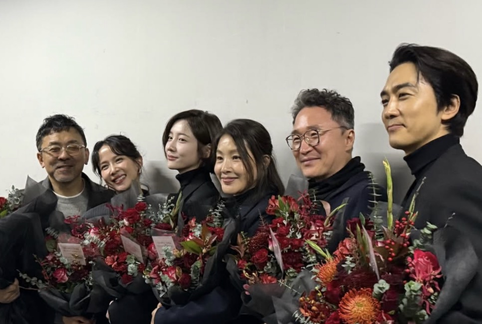 Park Ji-hyun ao lado de outros integrantes de uma produção, todos com buquês de flores