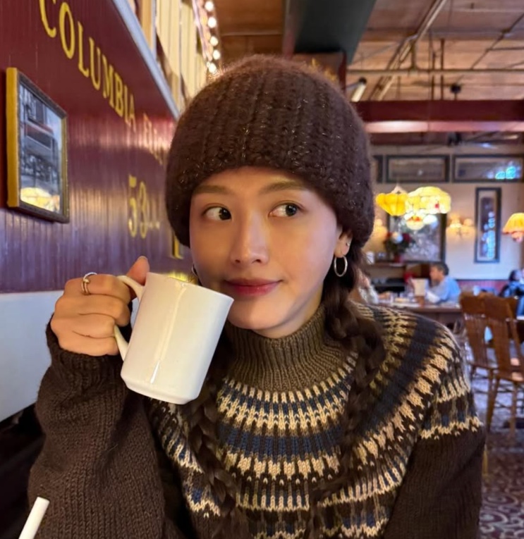Kim Jae-kyung de gorro de tricô, tomando café numa mesa de bar