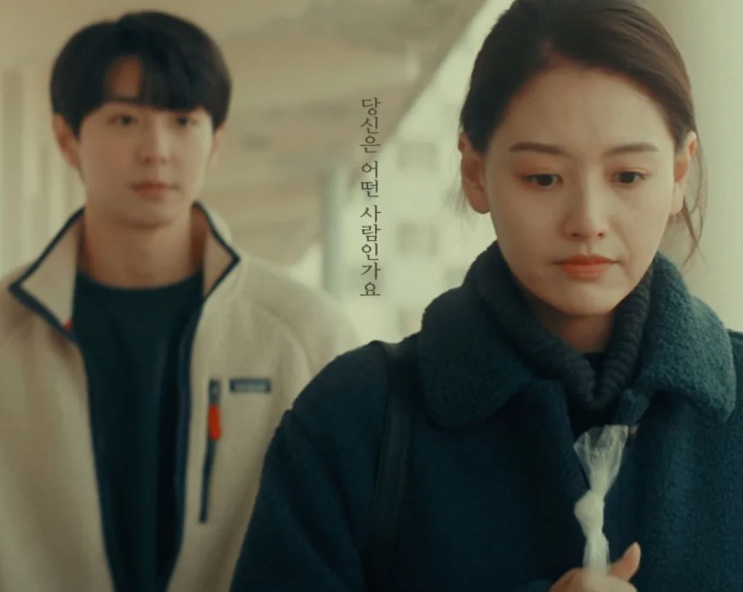 Woo-jae e Ji-su lado a lado num corredor, com uma frase em coreano na parede entre eles