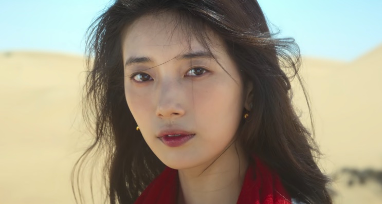 Ki Ga-young de blusa branca e lenço vermelho, com o cabelo ao vento no deserto