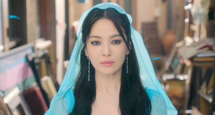 Song Hye-kyo de véu azul-turquesa e brincos longos, em uma rua de mercado