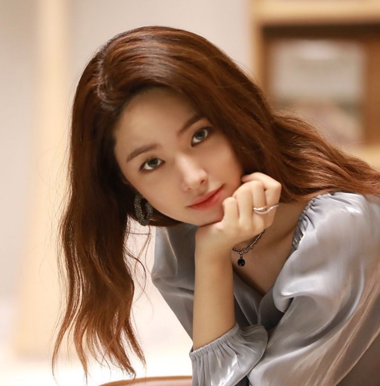 Ha Young com o cabelo castanho, apoiada na mão