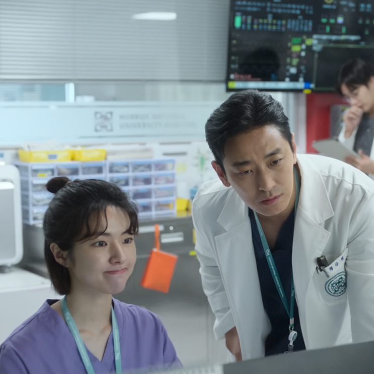 Baek Kang-hyuk e Cheon Jang-mi diante dos monitores, em Heróis de Plantão