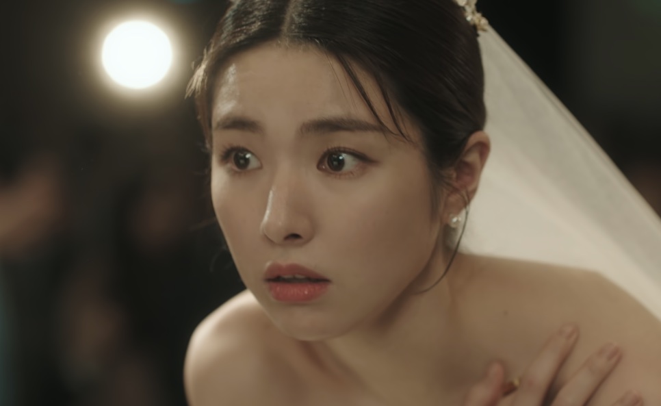 A noiva Kim Hwa-young segurando o vestido junto ao peito, com o rosto assustado, durante a entrada