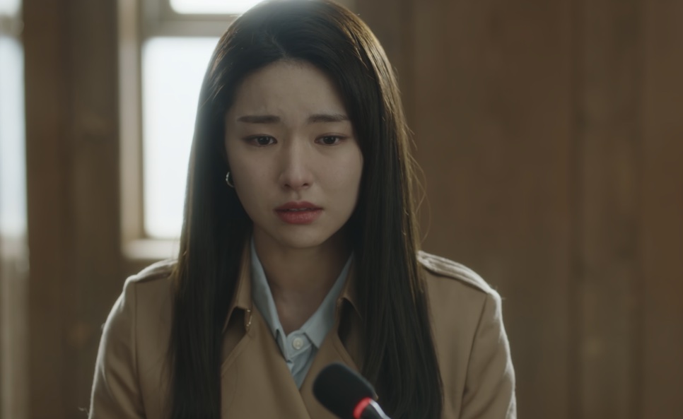 Kim Hwa-young depondo diante de um microfone, de casaco bege, em uma sala clara