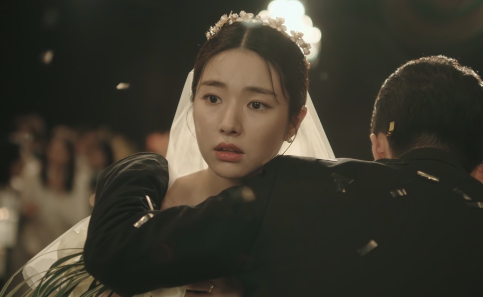 A noiva Kim Hwa-young abraçando um homem de terno no meio do salão, com os convidados ao fundo