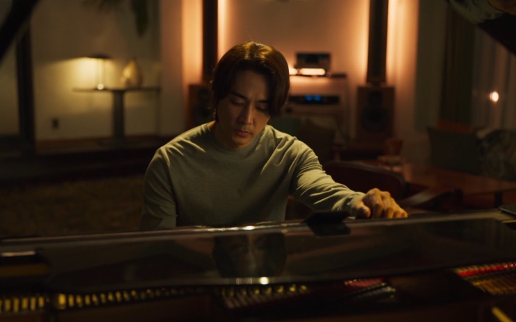 Song Seung-heon sentado ao piano de cauda, numa sala com luz baixa