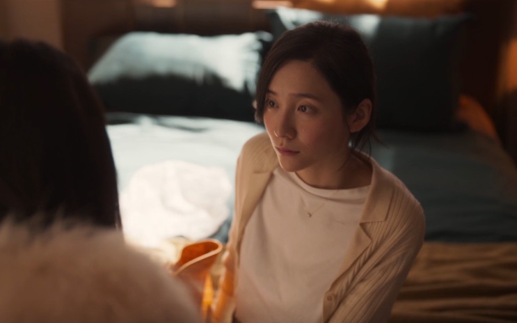 Cho Yeo-jeong de cardigã claro, sentada no chão ao lado de uma cama