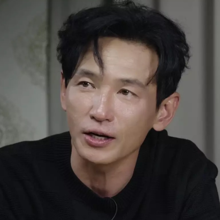 Hwang Jung-min de suéter preto, falando durante uma entrevista
